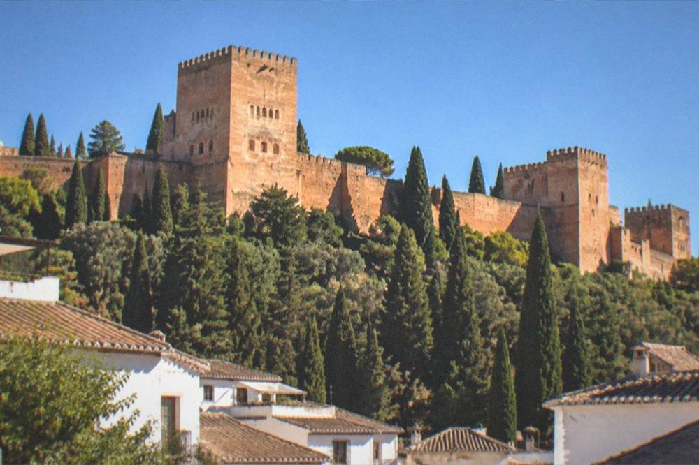 The Comares tower of the Alhambra rising above cypress trees with Granada rooftops below