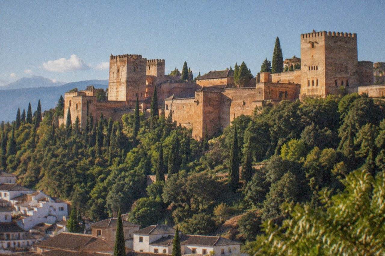 The Alhambra palace complex seen from a hillside viewpoint across the city of Granada at golden hour