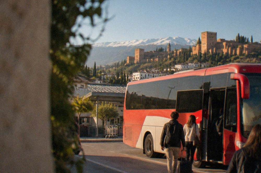 A red and white Alsa airport bus parked at Granada Airport with passengers boarding