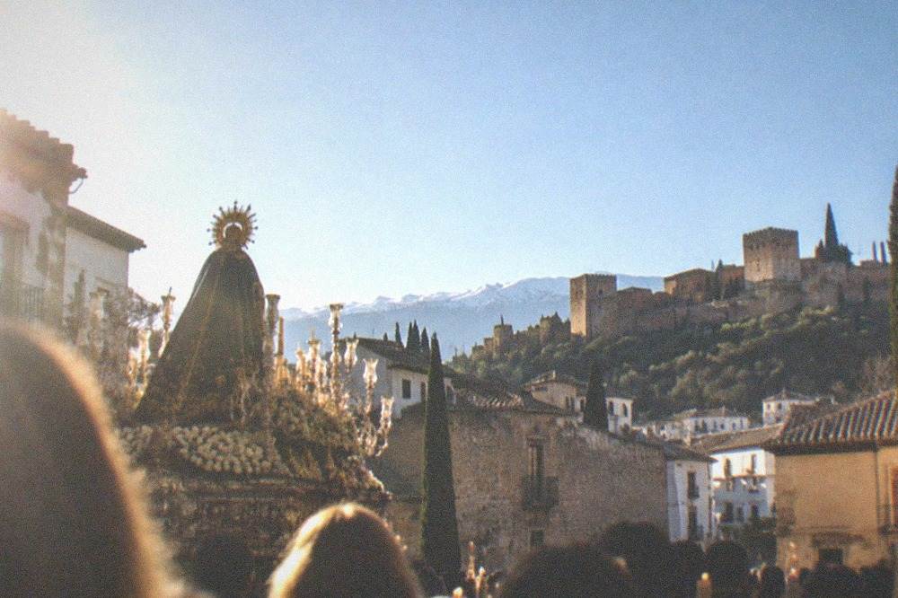 A procession crowd in a Granada square during Holy Week with candles and banners in the evening