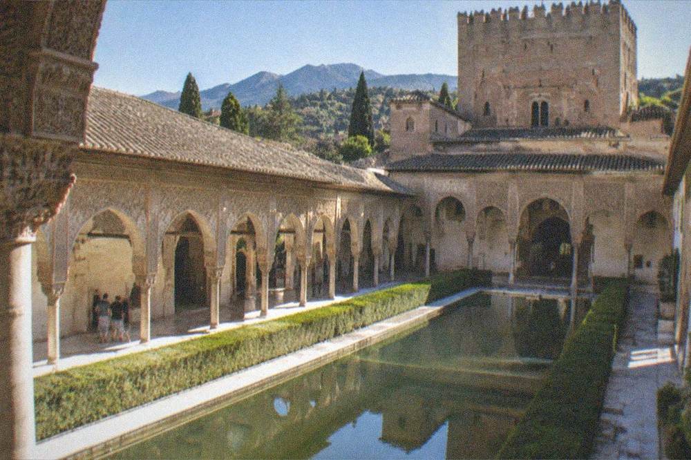The illuminated Nasrid Palaces of the Alhambra at night with the Sierra Nevada silhouette behind