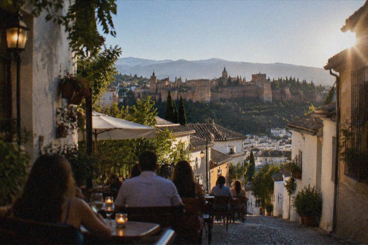Outdoor restaurant tables on a narrow Granada street in the evening with diners and warm lights
