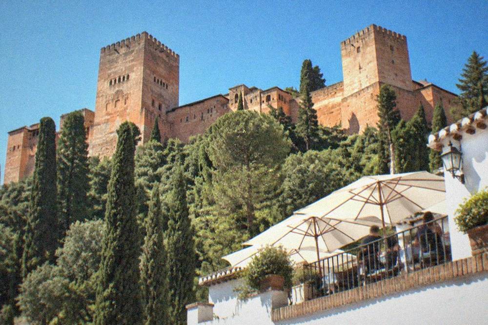 A white-walled restaurant terrace in the Albaicin overlooking the illuminated Alhambra after dark