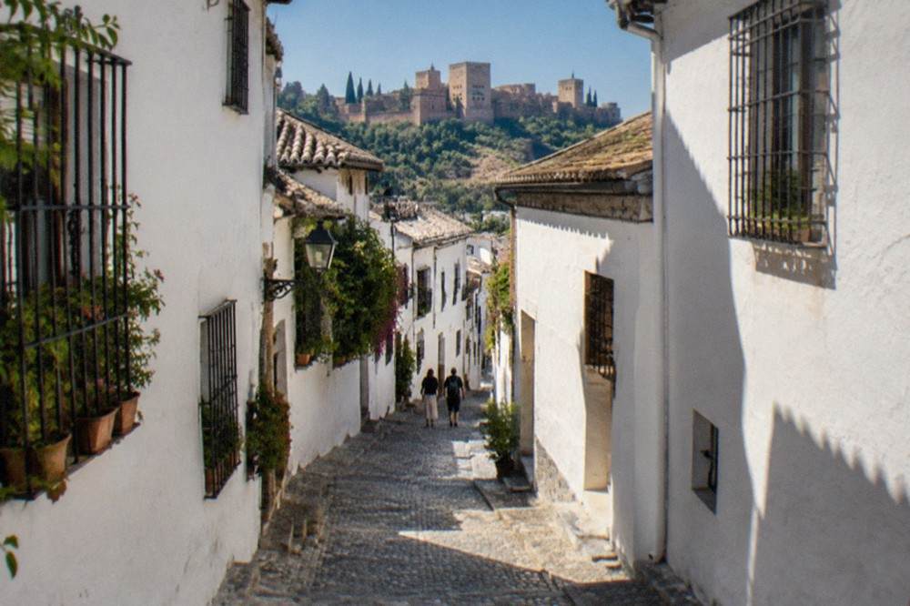 Narrow cobbled street in the Albaicin district with whitewashed houses under a clear blue sky