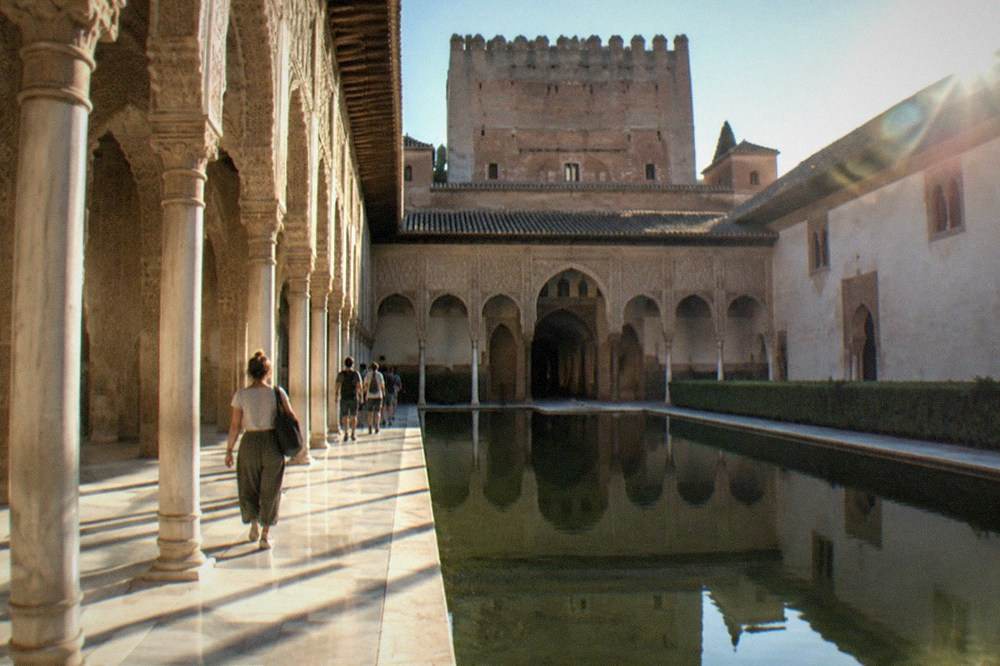 Visitors walking through the arched courtyards of the Nasrid Palaces in morning light