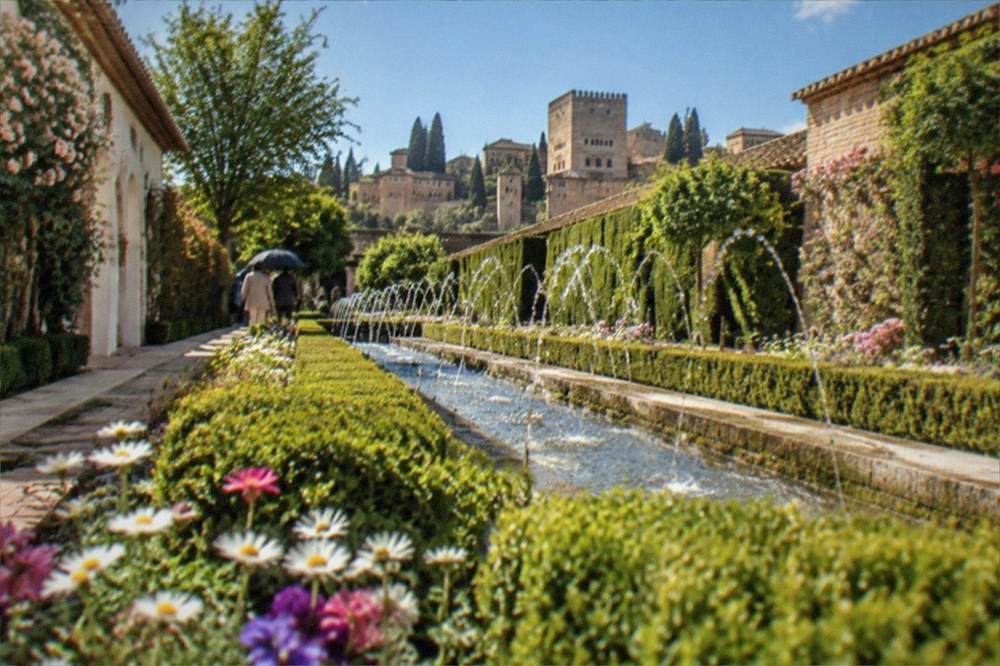 Spring flowerbeds and trimmed hedges along a walkway in the Generalife gardens