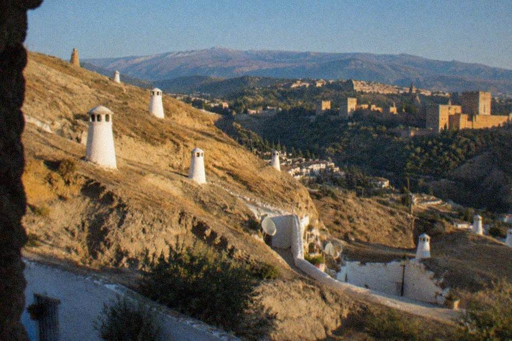 White cave houses on the hillside of Sacromonte at dusk with the Alhambra lit across the valley