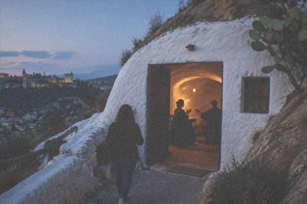 A singer clapping beside a guitarist in a small cave room with an arched ceiling