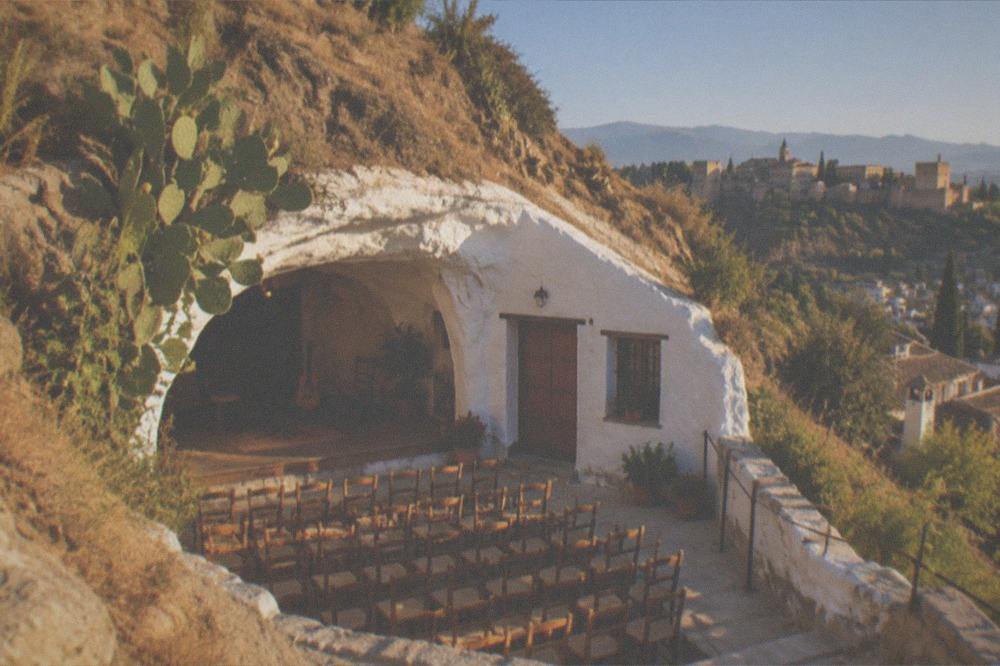 Rows of simple wooden chairs set up close together in a small cave venue before a performance