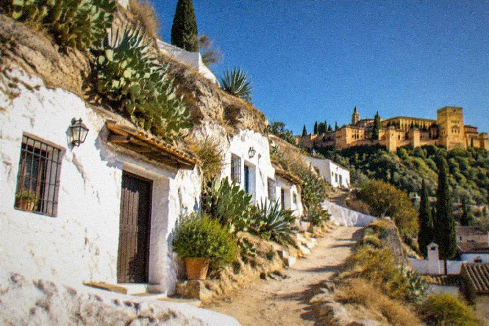 An evening view from a Sacromonte terrace toward the illuminated Alhambra under a deep blue sky