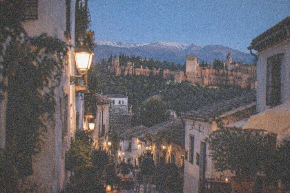 A narrow pedestrian tapas street in Granada at dusk with tables outside small bars