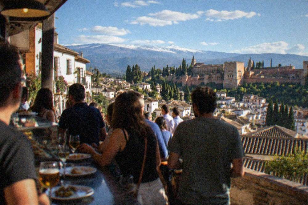 People standing at a crowded Granada bar counter holding small plates and drinks in the evening