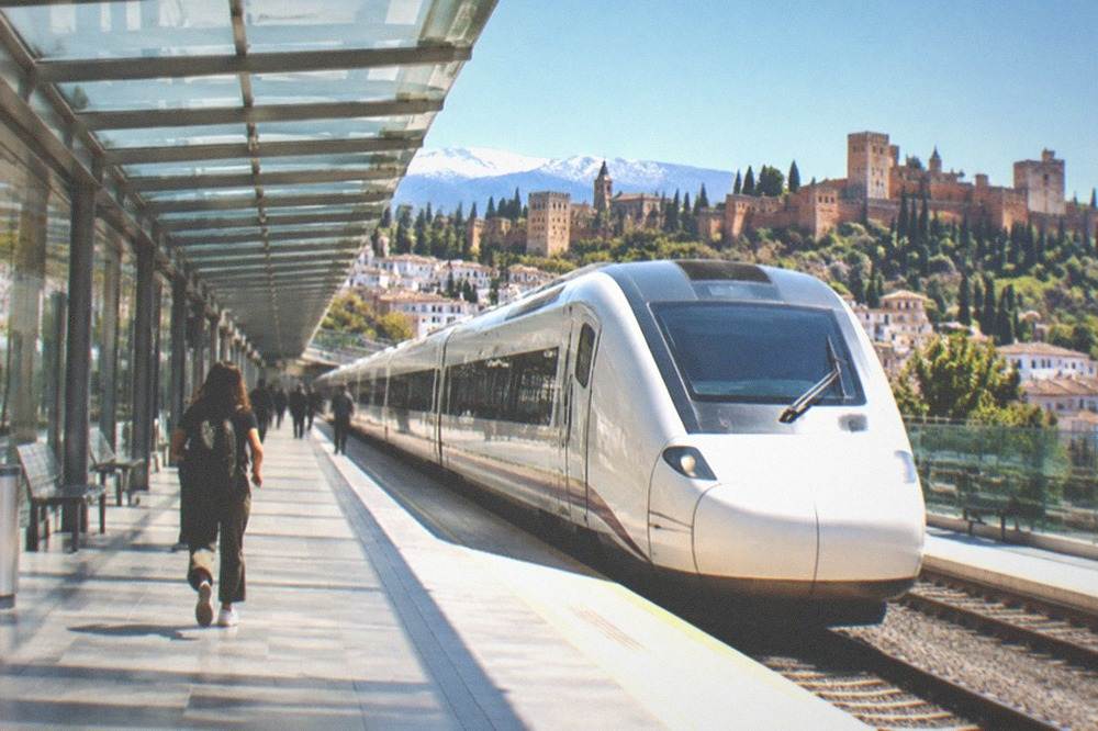 A sleek white high-speed train waiting at a platform under a canopy of glass and steel