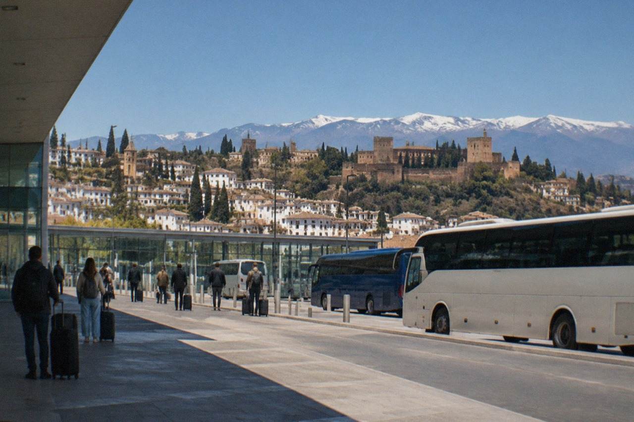 Buses parked at a modern bus station with glass doors and passengers waiting with luggage