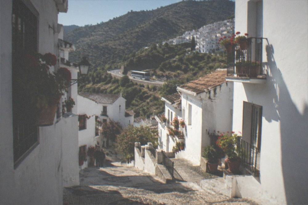 A coach driving along a mountain road with white villages clinging to green hillsides