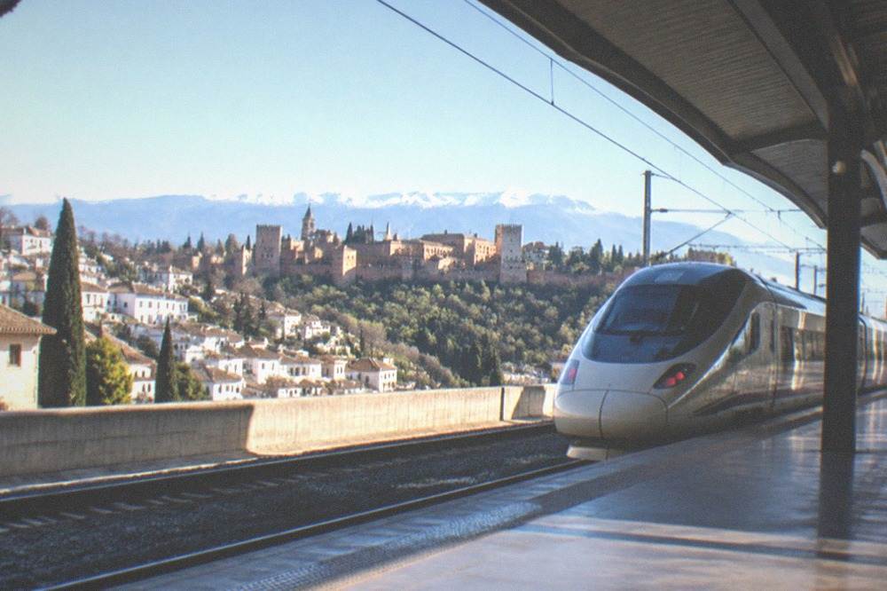A high-speed train waiting at a platform under a curved station roof