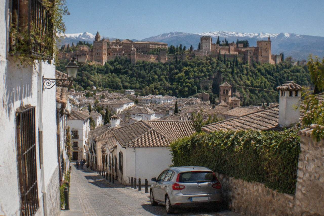 A rental car parked on a narrow street in Granada with the Alhambra visible on the hillside above the city