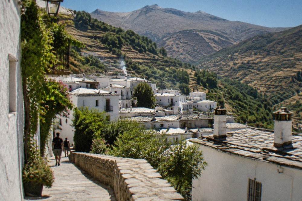 A white mountain village in the Alpujarras with terraced slopes behind it under a clear sky