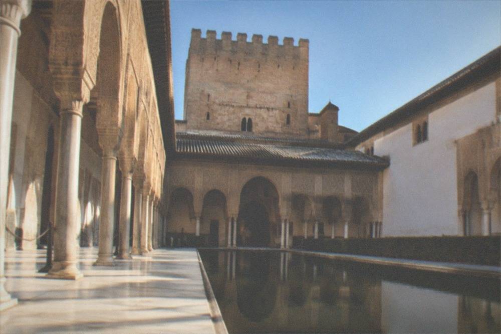 The courtyard of the Nasrid Palaces in the Alhambra with ornate arches and a reflecting pool