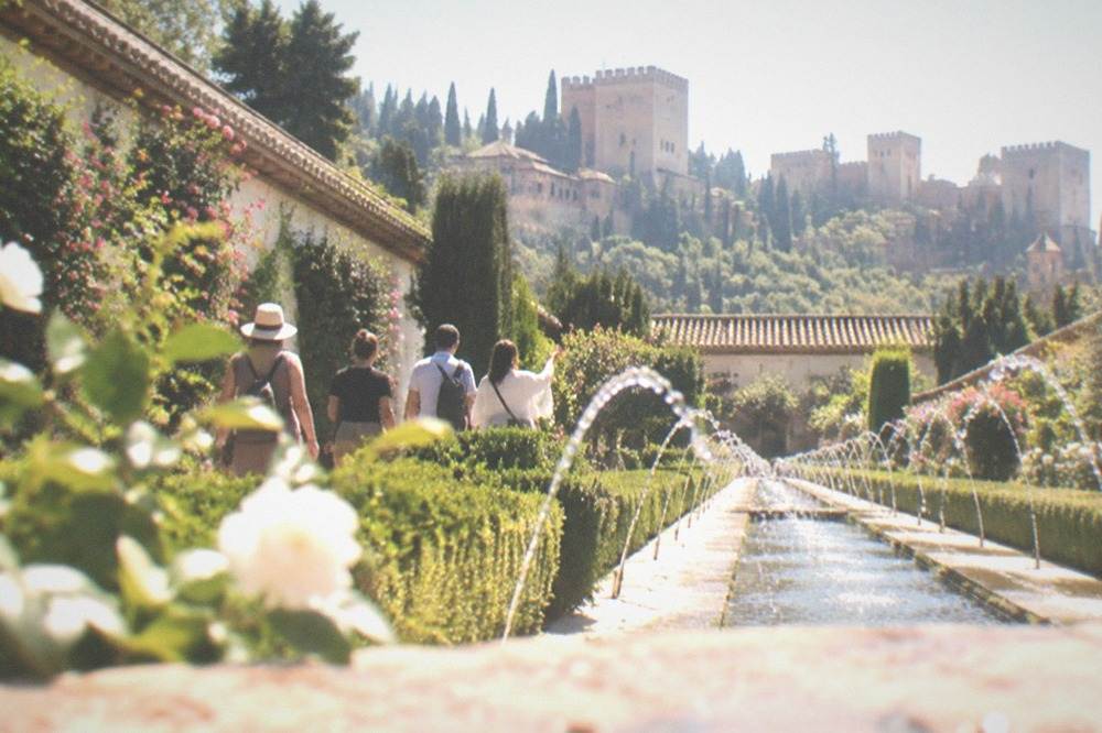 A small group of visitors with a guide walking through the Generalife gardens at the Alhambra