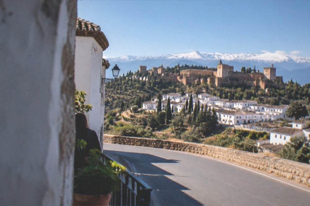 An empty mountain road curving toward the white villages of the Alpujarras under the Sierra Nevada