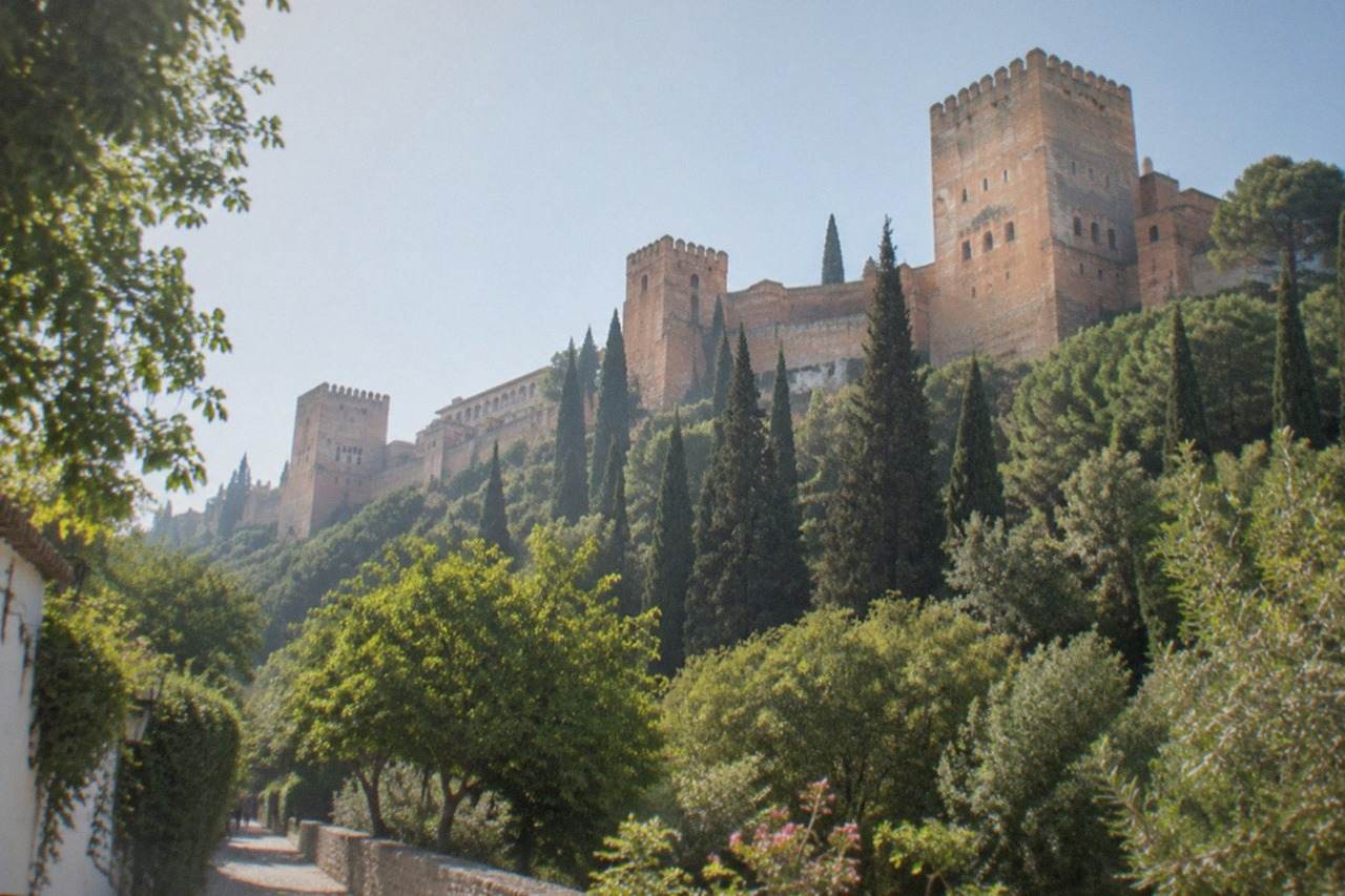 The Alhambra palace complex seen from a leafy garden path in Granada on a bright morning