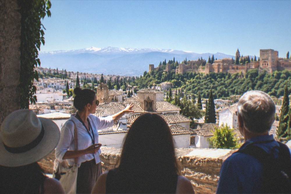 A guide speaking to a small group of visitors on a sunlit terrace overlooking Granada