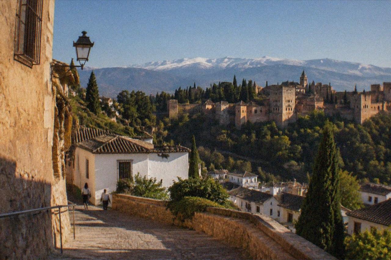 Illuminated historic buildings in Granada at dusk with the Sierra Nevada visible in the distance
