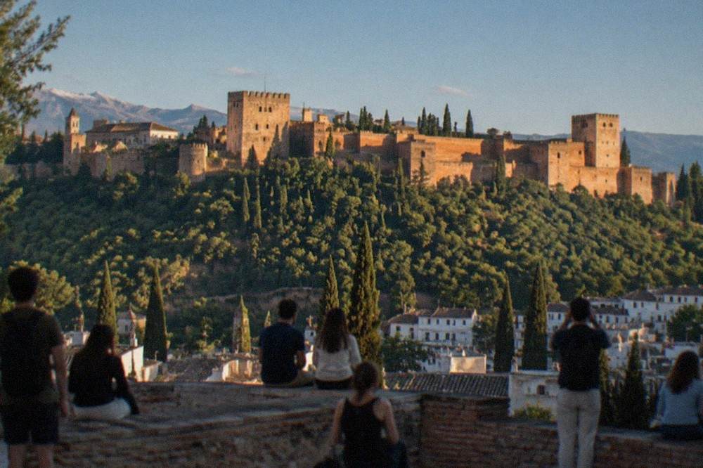 People gathered at a hillside viewpoint watching the sunset over the Alhambra