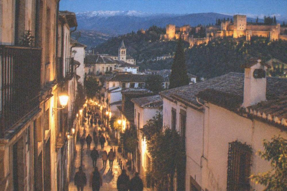 A lit pedestrian street in the old town of Granada with people walking at night