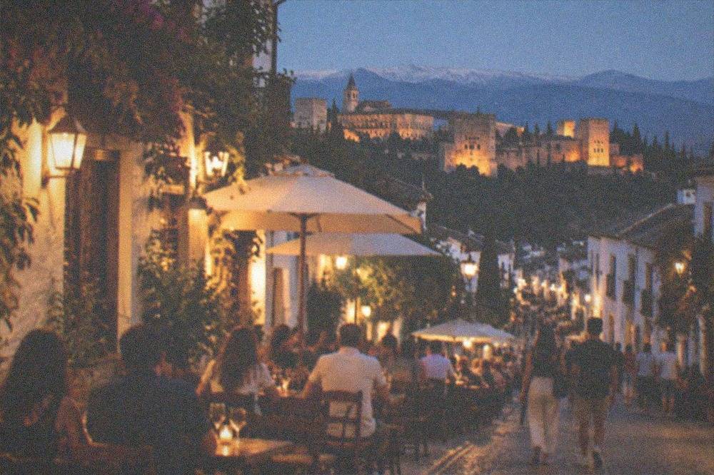A busy tapas street in central Granada at night with outdoor tables and warm lighting
