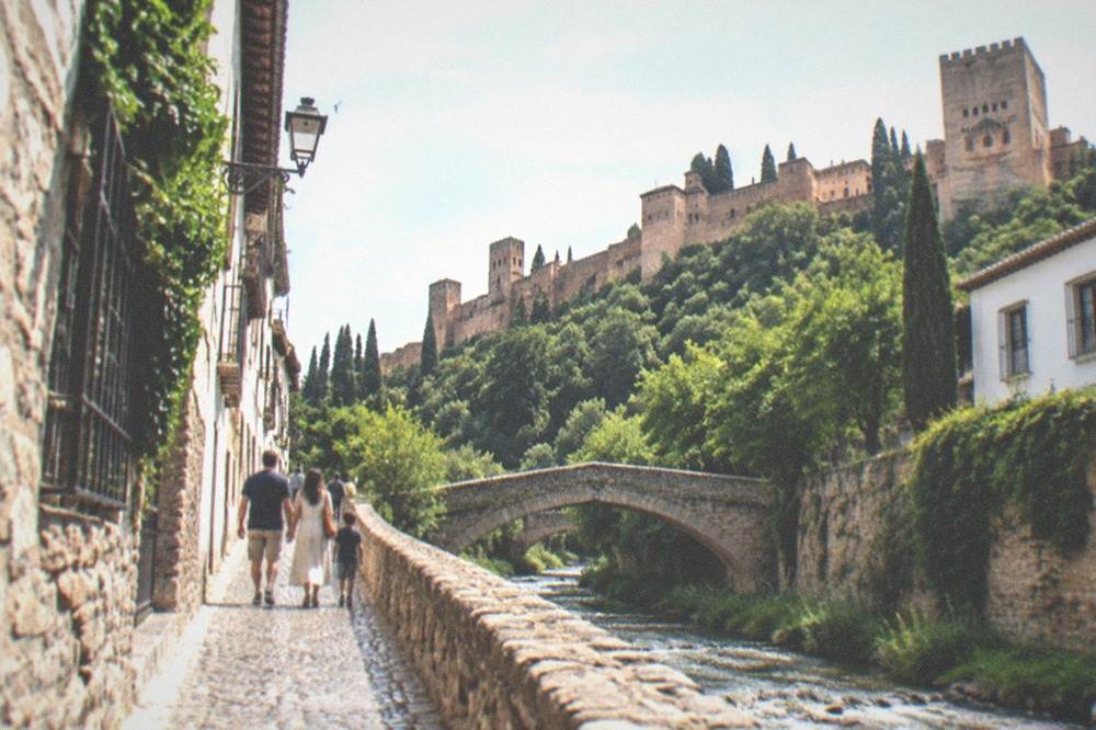 A family walking along the riverside Carrera del Darro with the Alhambra towers above