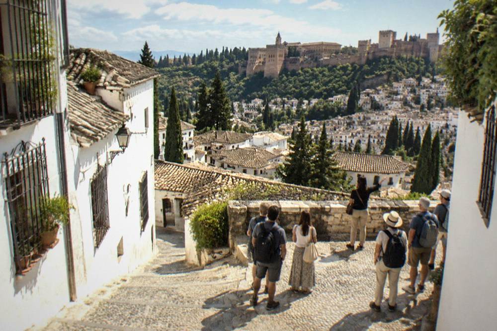 Visitors and a guide standing on a plaza overlooking the Albaicin rooftops toward the Alhambra