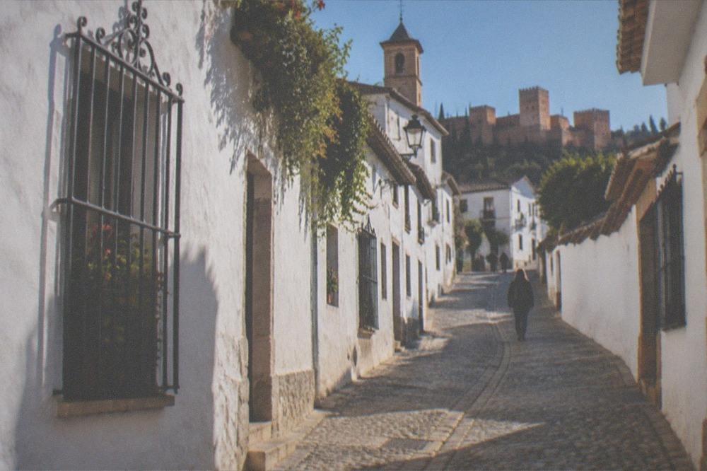 A narrow cobbled street in the Albaicin with white houses and a church tower above