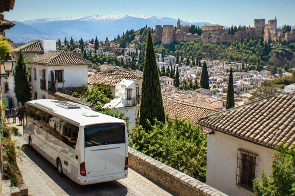 A tour coach parked on a street with historic Andalusian buildings in the background