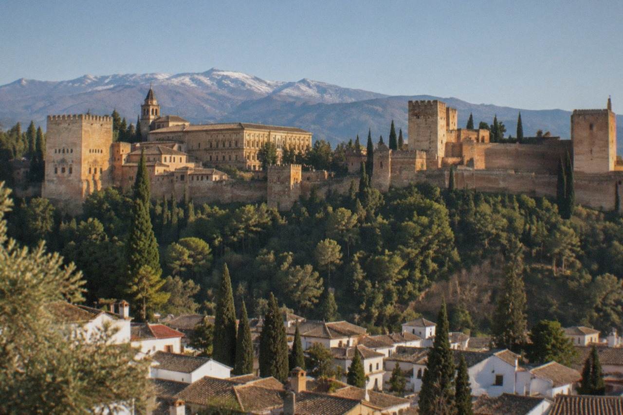 The Alhambra palace complex on its hill above the red rooftops of Granada with mountains in the distance