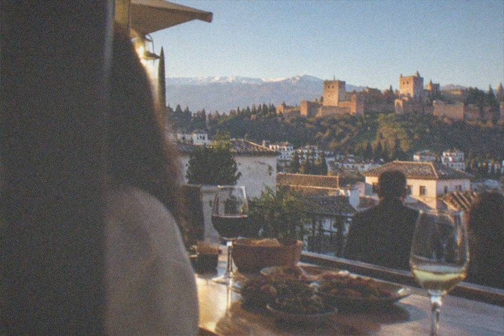 A wooden bar top with small tapas plates, olives and glasses of Spanish wine in a busy Granada bar