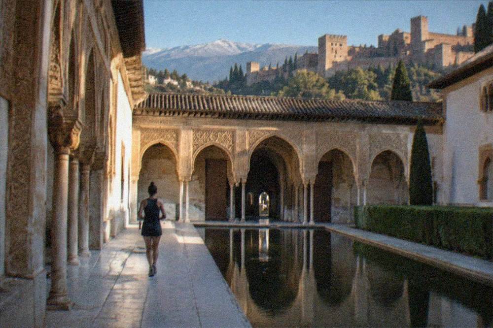 The ornate carved arches and stucco walls of a Moorish palace courtyard with light reflecting on water