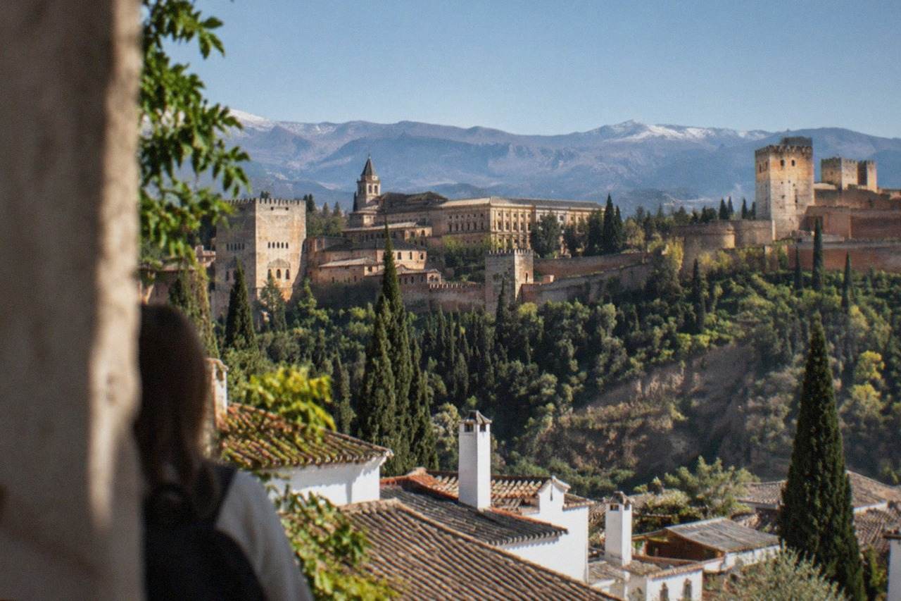 The Alhambra palace complex on its hill above the red rooftops of Granada with mountains in the background