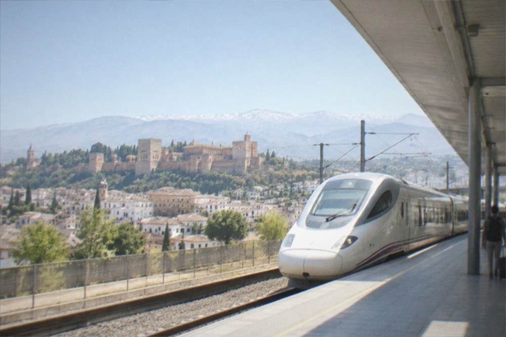 A high-speed train waiting at a platform under a modern station roof in Spain