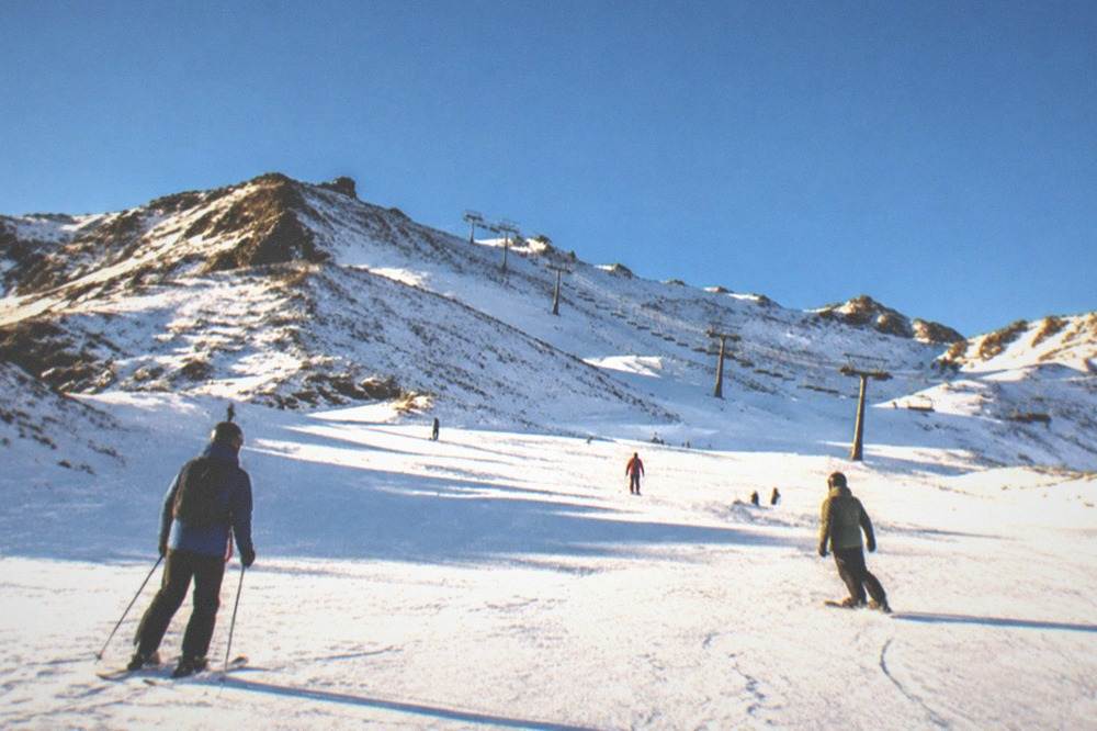 Skiers and snowboarders on a wide piste under sunshine in the Sierra Nevada above Granada