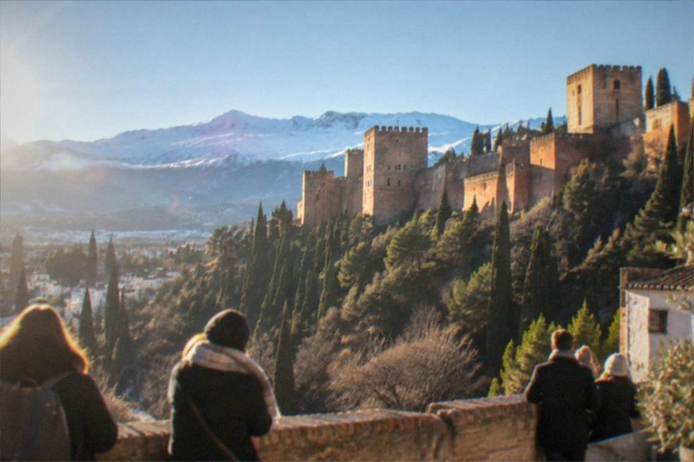 Visitors on a terrace of the Alhambra looking toward snow-dusted mountains on a bright clear morning