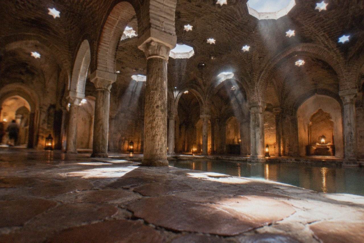 Warm candlelit interior of an ornate Arab bath house with arched doorways and a stone pool