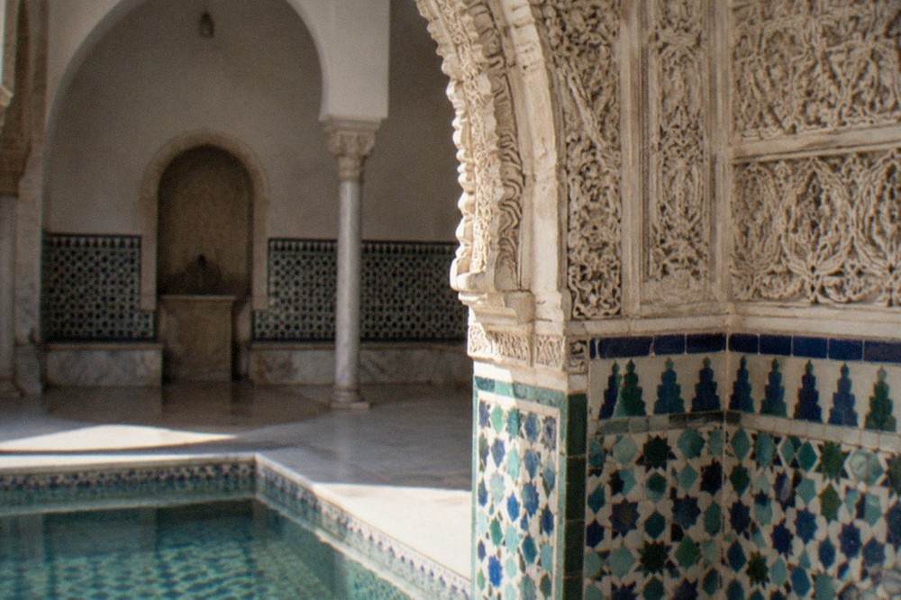 Detail of glazed blue and green tiles and a carved plaster arch inside a Granada bath house