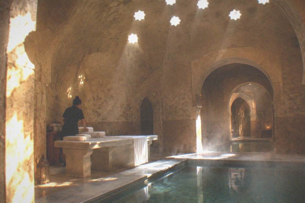 A therapist preparing towels beside a marble massage platform in a softly lit hammam