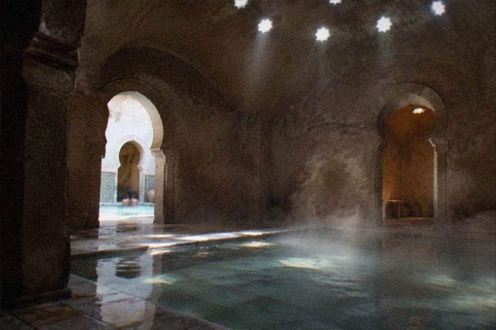 Steam rising from a hot pool in a tiled hammam room lit by small ceiling skylights