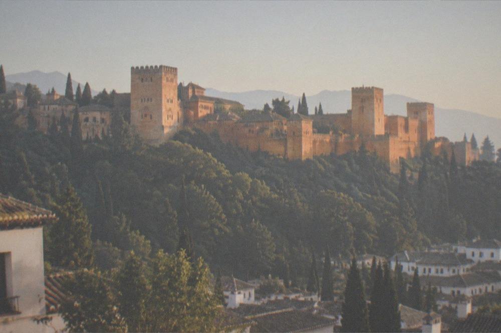 The Alhambra glowing above the city at sunset seen from a hillside square