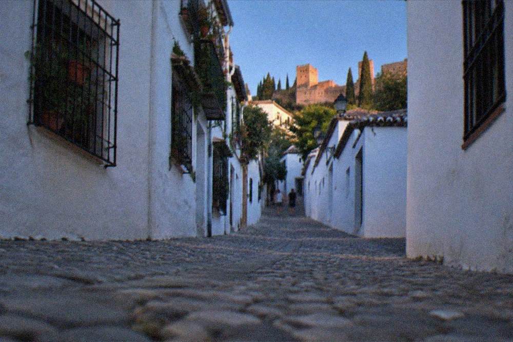 A narrow street in the Albaicin with white houses under a clear blue sky