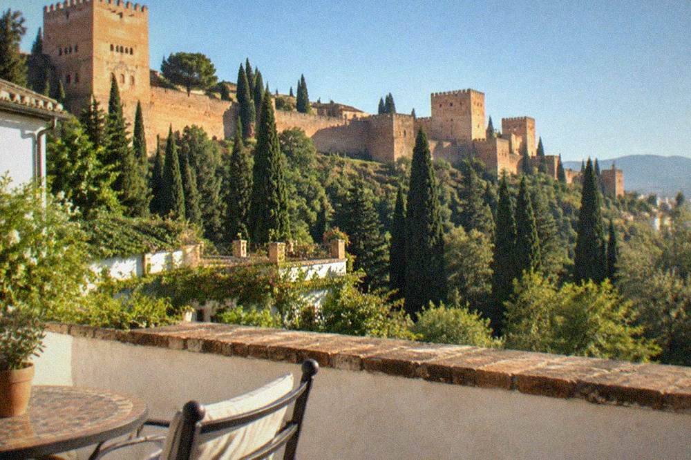 A quiet hotel terrace overlooking gardens and red-walled towers at dusk