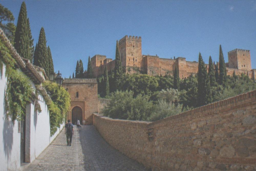 A stone-paved cobbled lane climbing between high walls toward a fortress gate